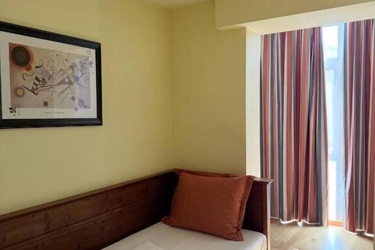 A single bed with a wooden headboard and a brown pillow in a room with a light-colored wall and a framed picture.
