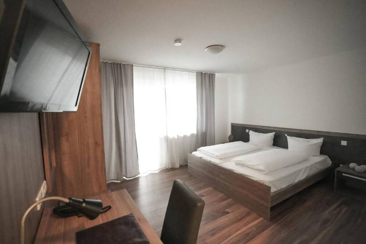 A hotel room with a bed, a desk, a chair, a TV, and a window with curtains.