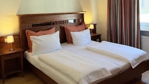 A hotel room with a large bed, two bedside tables with lamps, a wooden headboard, and a window with curtains. - Hotel Altavilla (Schwetzingen)