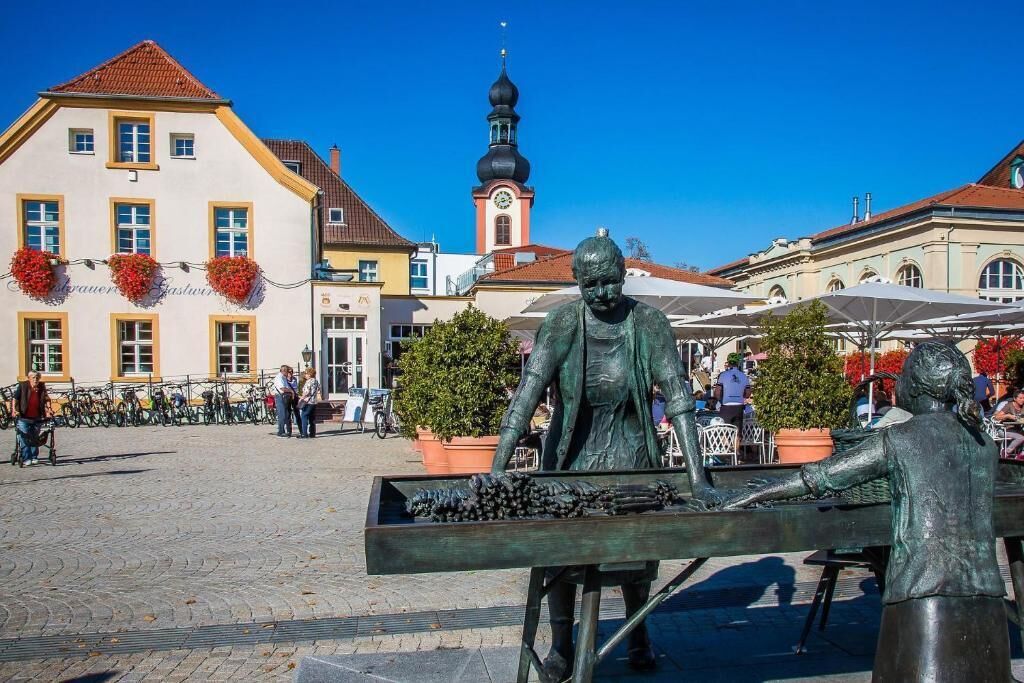 Ett offentligt torg med en staty, byggnader och ett klocktorn.