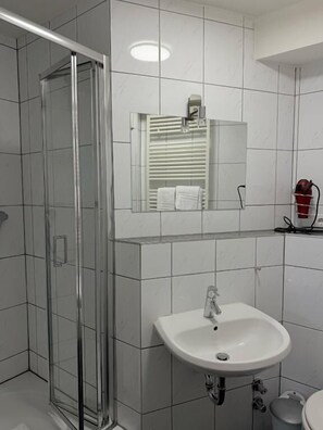 Un baño con cabina de ducha de vidrio, un lavabo blanco y un espejo sobre el lavabo.