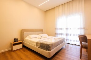 A bedroom with a bed, bedside table, chair, and a window with curtains. - Toro Double Room with City View (Durrës)