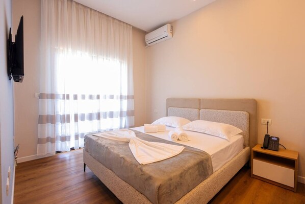 A hotel room with a bed, a bedside table with a phone, and an air conditioning unit. - Toro Family Room with City view (Durrës)