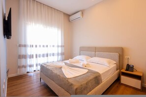 Ein Hotelzimmer mit Bett, Nachttisch mit Telefon, Wandfernseher und Klimaanlage.