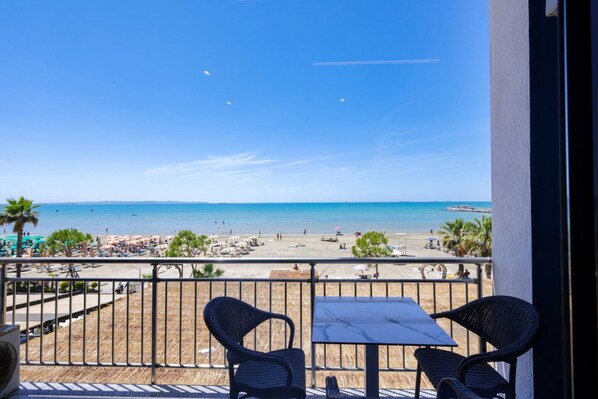 Ein Balkon mit zwei Stühlen und einem Tisch mit Blick auf einen Strand mit Sonnenschirmen und Menschen.