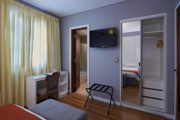 A hotel room with a bed, a desk, a chair, a TV, a wardrobe, and a small stool. - Altos de Güemes Hotel (Mar del Plata)