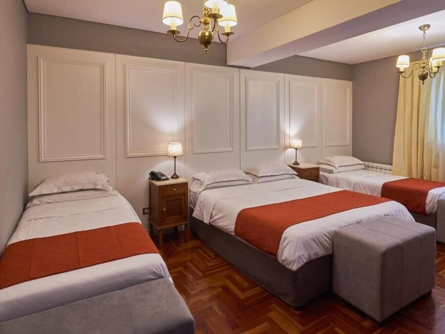 A hotel room with three beds, wooden flooring, and a chandelier.