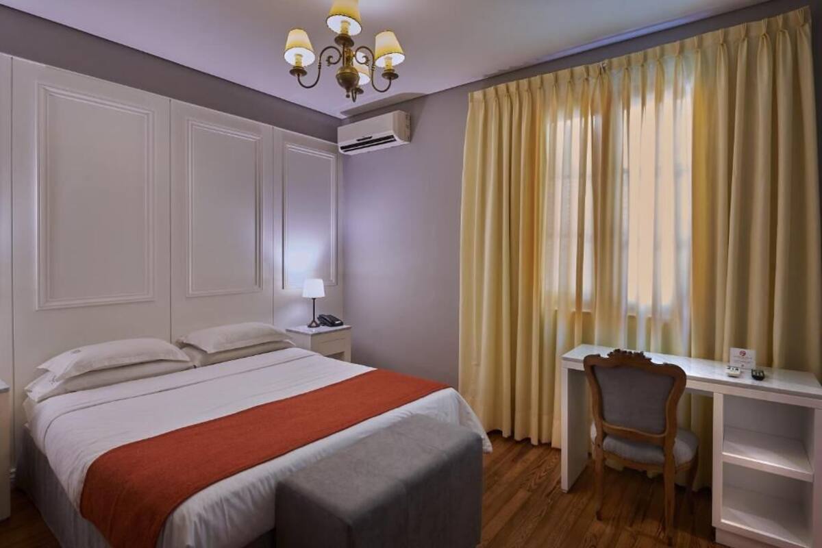 A hotel room with a bed, desk, chair, and curtains.
