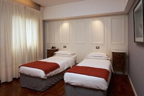 Ein Hotelzimmer mit zwei Betten, Holzboden, weißem Vorhang und einem gerahmten Bild an der Wand.
