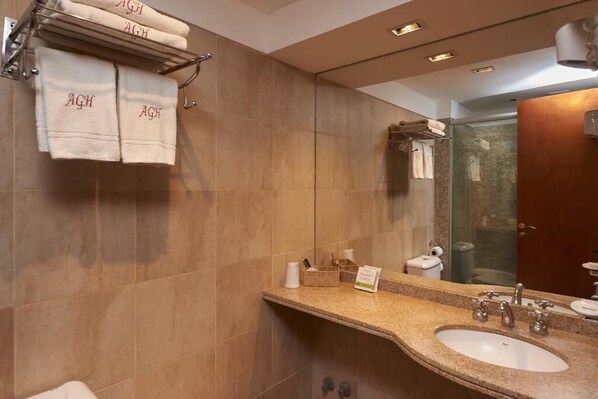 A modern bathroom with a granite countertop, two sinks, a towel rack with towels, and a mirror.
