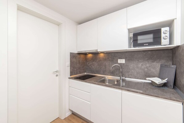 A compact kitchen with white cabinets, a stainless steel sink, a microwave, and a small basket. - Altiora Prestige Residence 303 (Gradac)