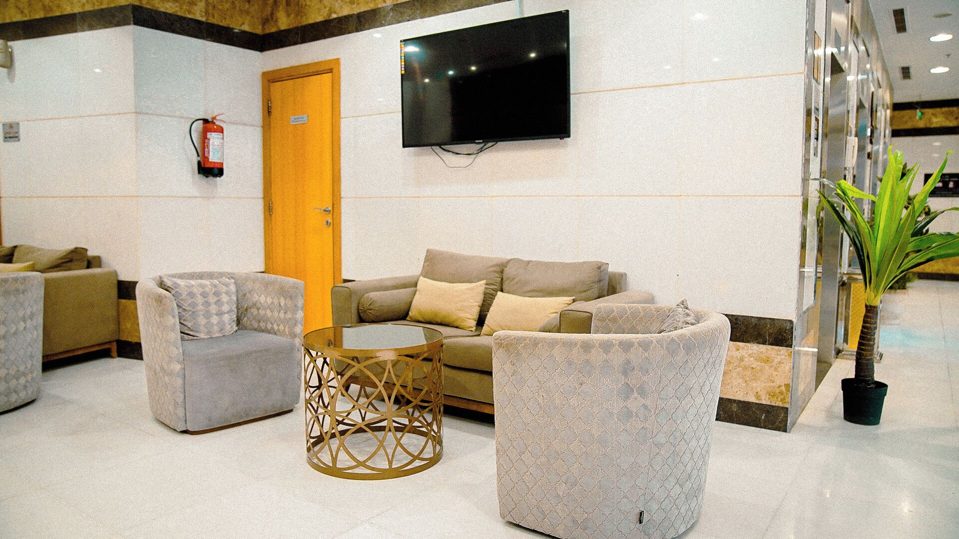 A lobby with a sofa, armchairs, a coffee table, a television, and a fire extinguisher.
