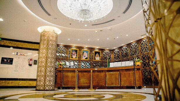 Un vestíbulo con una gran lámpara de cristal, un mostrador de recepción y un pilar decorativo.