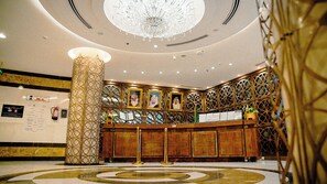 Un hall d’entrée avec un grand lustre, un comptoir d’accueil et un pilier décoratif.