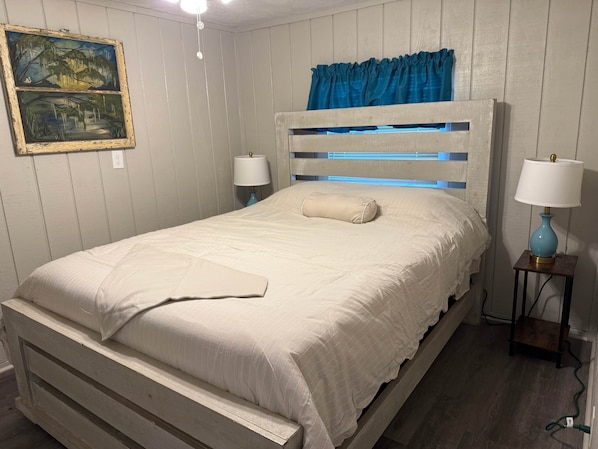 Ein Bett mit Kopfteil, zwei Nachttischlampen, ein Nachttisch, ein an der Wand hängendes Gemälde und eine Deckenleuchte.