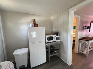 Eine kompakte Küche mit Kühlschrank, Mikrowelle und einer kleinen Ablage für Küchenutensilien.