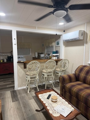 Un salon comprenant un canapé, une table basse avec une télécommande et des documents, ainsi qu’un coin repas avec des chaises et une table.