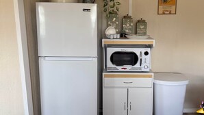 Una kitchenette compacta con refrigerador, microondas y un mueble pequeño.
