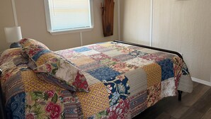Un dormitorio con cama, ventana con persianas, perchero de madera y espejos en la pared.