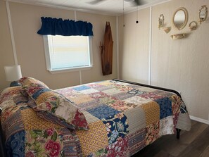 Une chambre à coucher avec un lit, une fenêtre avec des stores, un porte-manteau en bois et des miroirs fixés au mur.