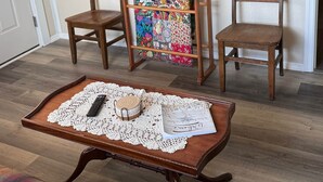 Una sala de estar con dos sillas de madera, una mesita con un posavasos de encaje, un colcha y un televisor de pantalla plana montado en la pared.