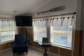 Ein Zimmer mit einem dunkelblauen Sessel, einem kleinen runden Tisch mit einem Laptop und einem an der Wand befestigten Fernseher.