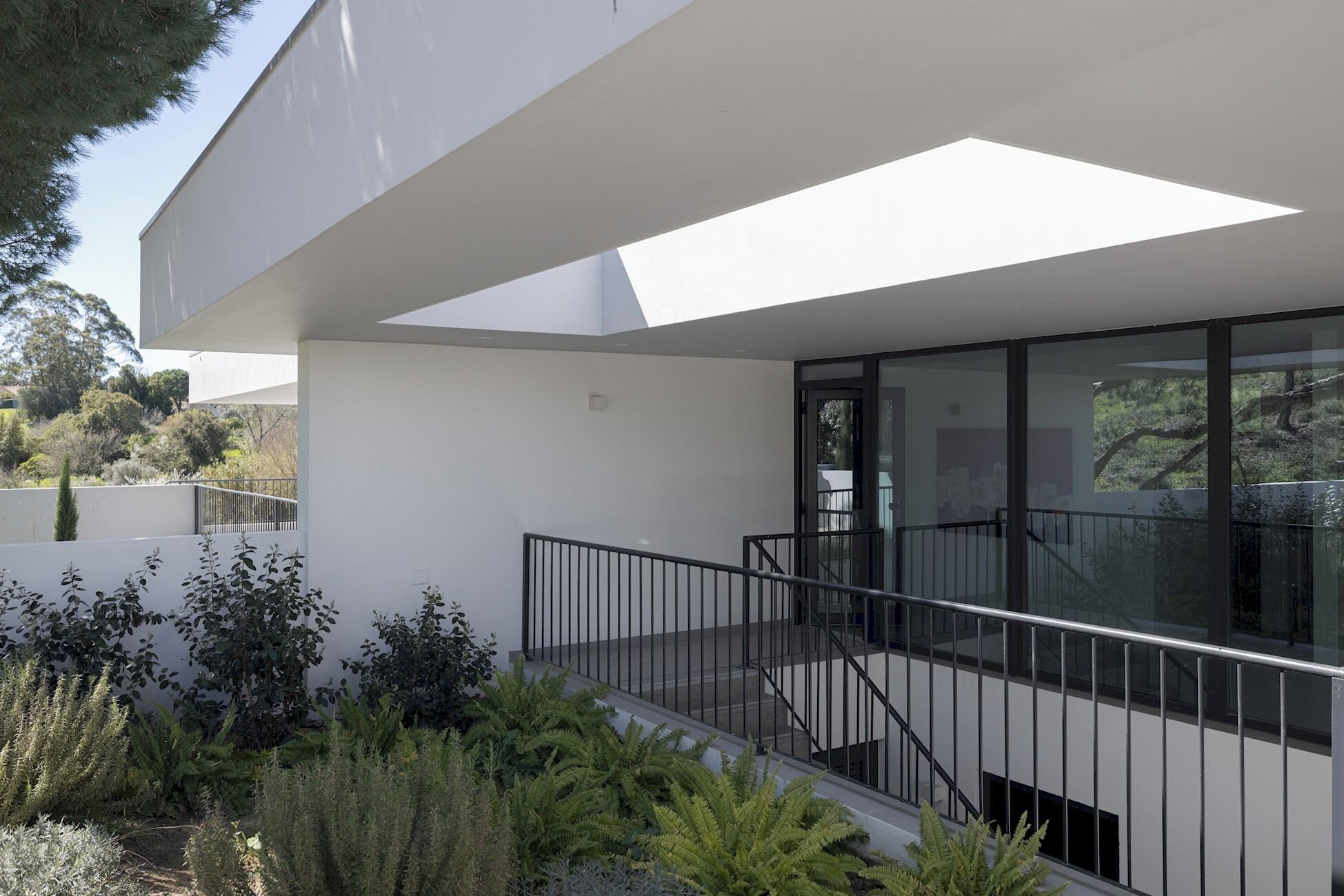 A modern building with a glass balcony, white walls, and a staircase leading to an upper level.