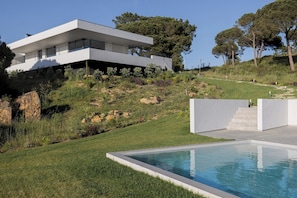 Ein modernes, zweistöckiges Haus mit Schwimmbad, umgeben von einem angelegten Garten und Bäumen.