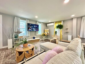 Ein modernes Wohnzimmer mit Flachbildfernseher, einer Couch, einem Couchtisch und einer Zierpflanze.