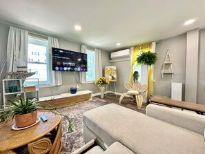 Ein modernes Wohnzimmer mit Flachbildfernseher, Sofa und Essbereich mit Tisch und Stühlen.