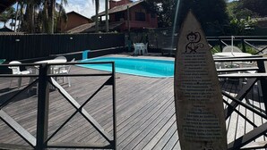 A pool area with a wooden deck, a sign with rules, and palm trees in the background. - recanto  (Garopaba)