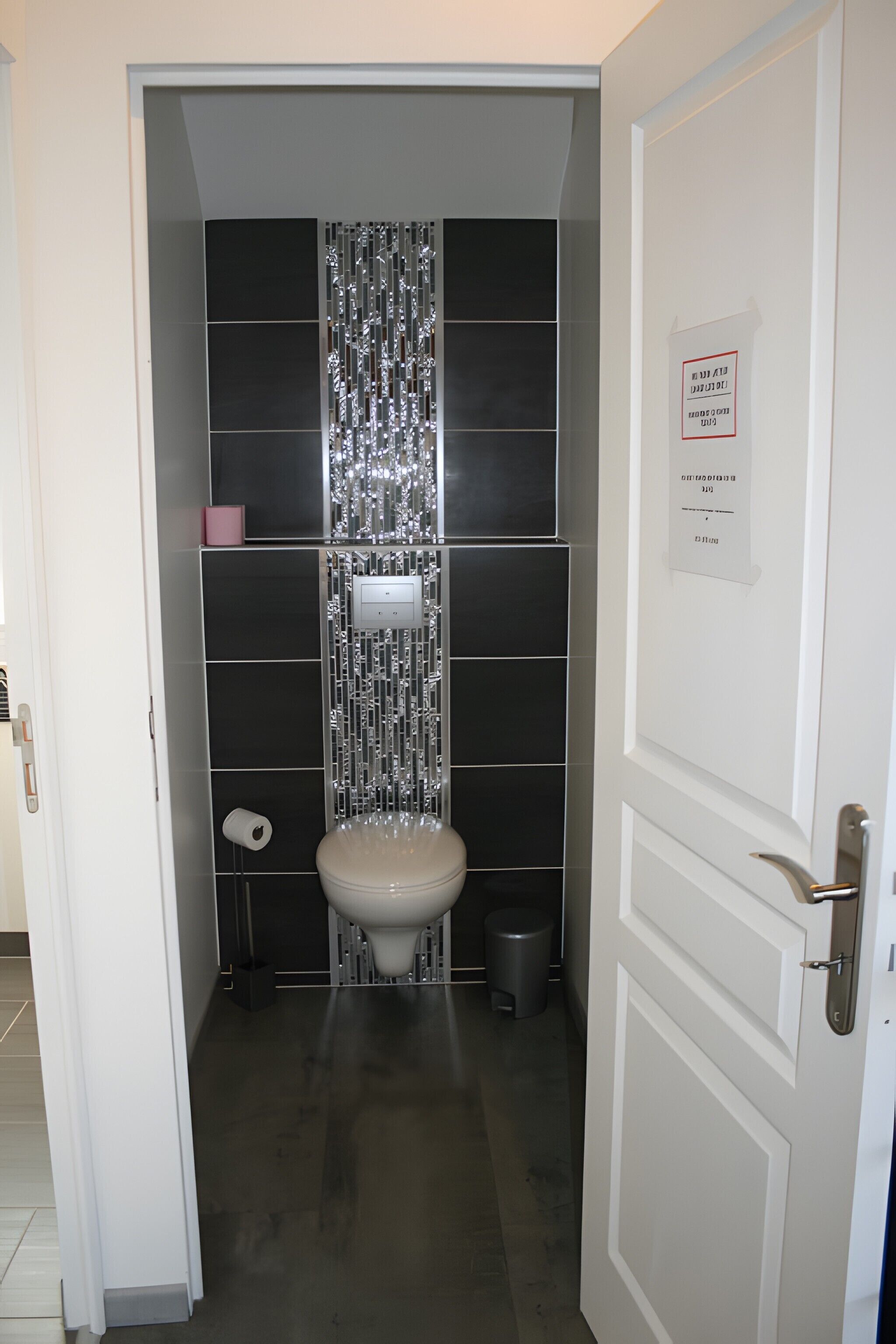 Een kleine badkamer met een toilet, een prullenbak en een toiletrol op de vloer.