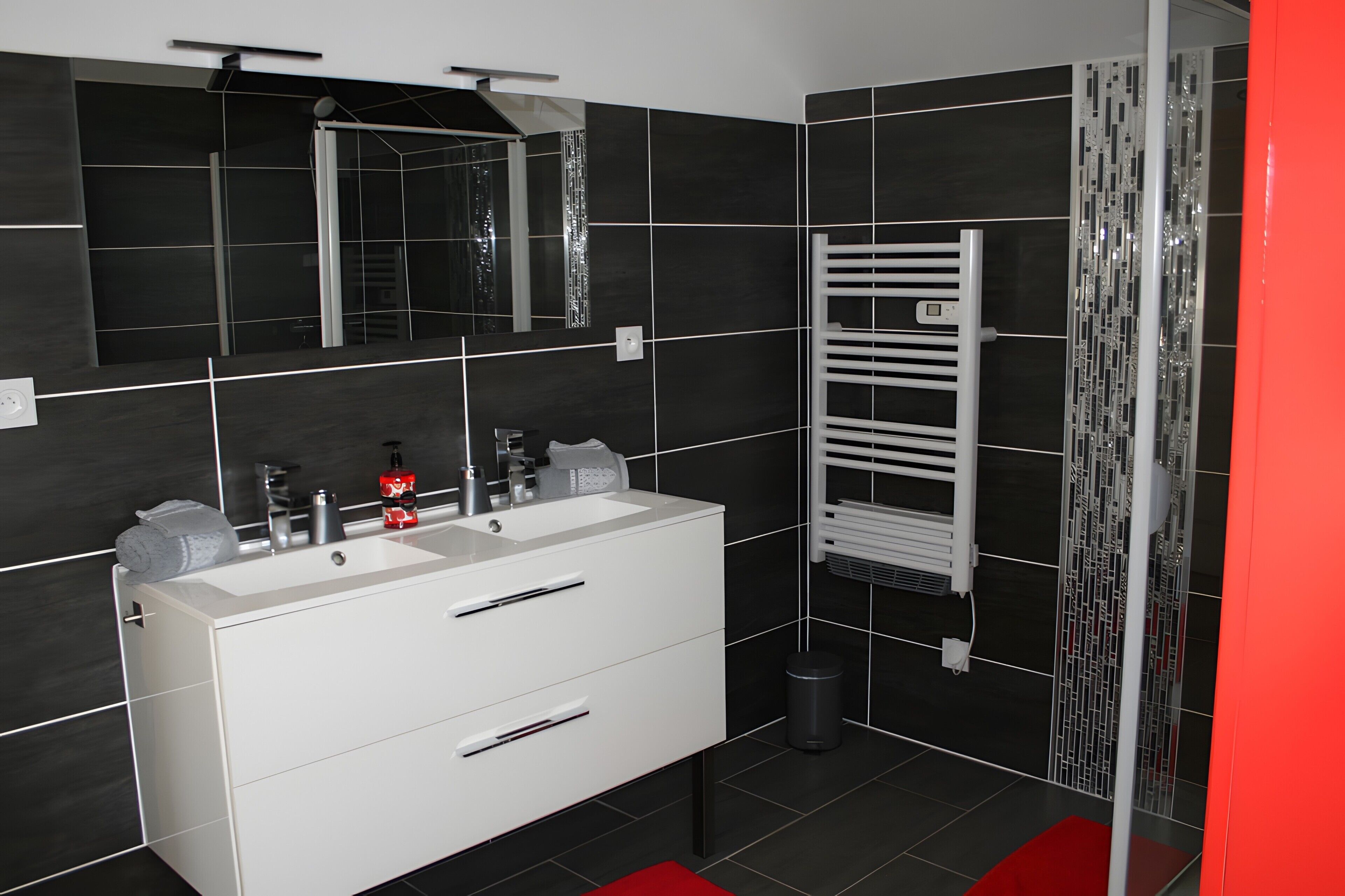 A modern bathroom with a double sink vanity, a mirror, a towel rack, and a shower area.
