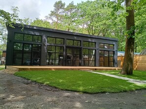 A modern building with large windows, a wooden deck, and a grassy area. - Luxe chalet midden in de natuur (Rijen)