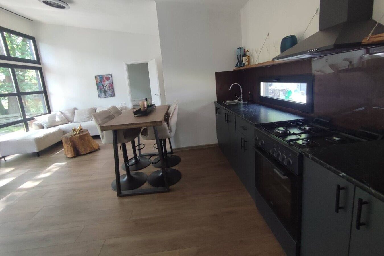 Moderni keittiö, jossa on ruokailutila, puulattia ja suuri ikkuna.