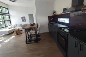 A modern kitchen with a dining area, wooden flooring, and a large window. - Luxe chalet midden in de natuur (Rijen)