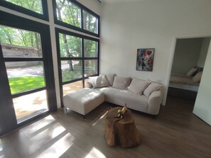 A modern living room with a sectional sofa, a wooden stump, and large windows. - Luxe chalet midden in de natuur (Rijen)