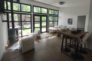 A spacious living room with large windows, a fireplace, a dining area, and a sofa. - Luxe chalet midden in de natuur (Rijen)