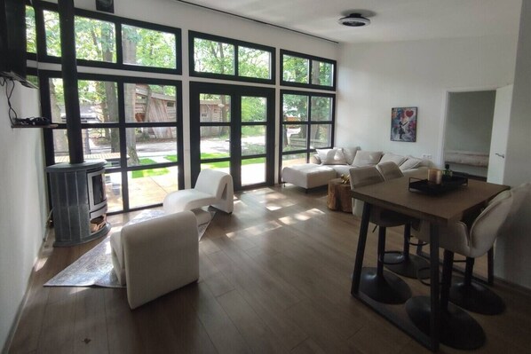A spacious living room with large windows, a fireplace, a dining area, and a sofa. - Luxe chalet midden in de natuur (Rijen)