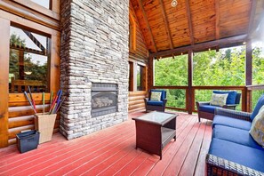 Eine Blockhütte mit Kamin aus Stein, Korbmöbeln und einer roten Holzterrasse.