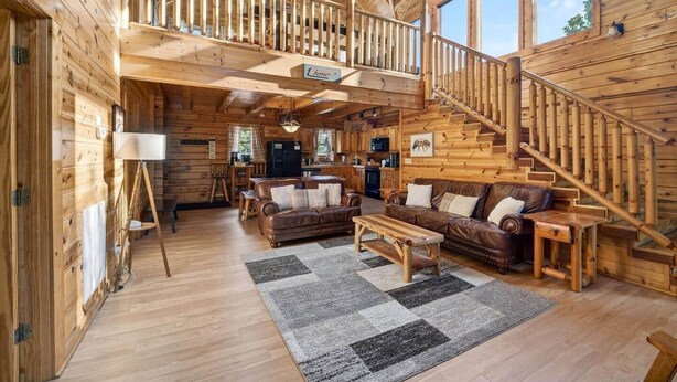 A log cabin interior with a staircase, a living room with a sofa and coffee table, and a kitchen area.