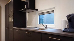 Cozinha moderna com armários escuros, forno embutido, janela com persianas e cafeteira sobre a bancada.