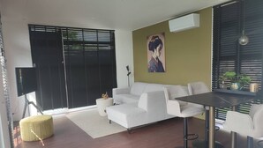 Uma sala de estar moderna com sofá, mesa de jantar e cadeiras, um banquinho amarelo e um quadro na parede.