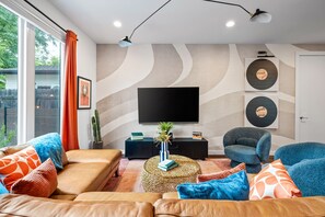 A modern living room with a large flat-screen TV, a comfortable sofa, a blue armchair, and a coffee table with decorative items. - Rainey Escape / Pool / Hot Tub / Fire Pit / DT ATX (Austin)