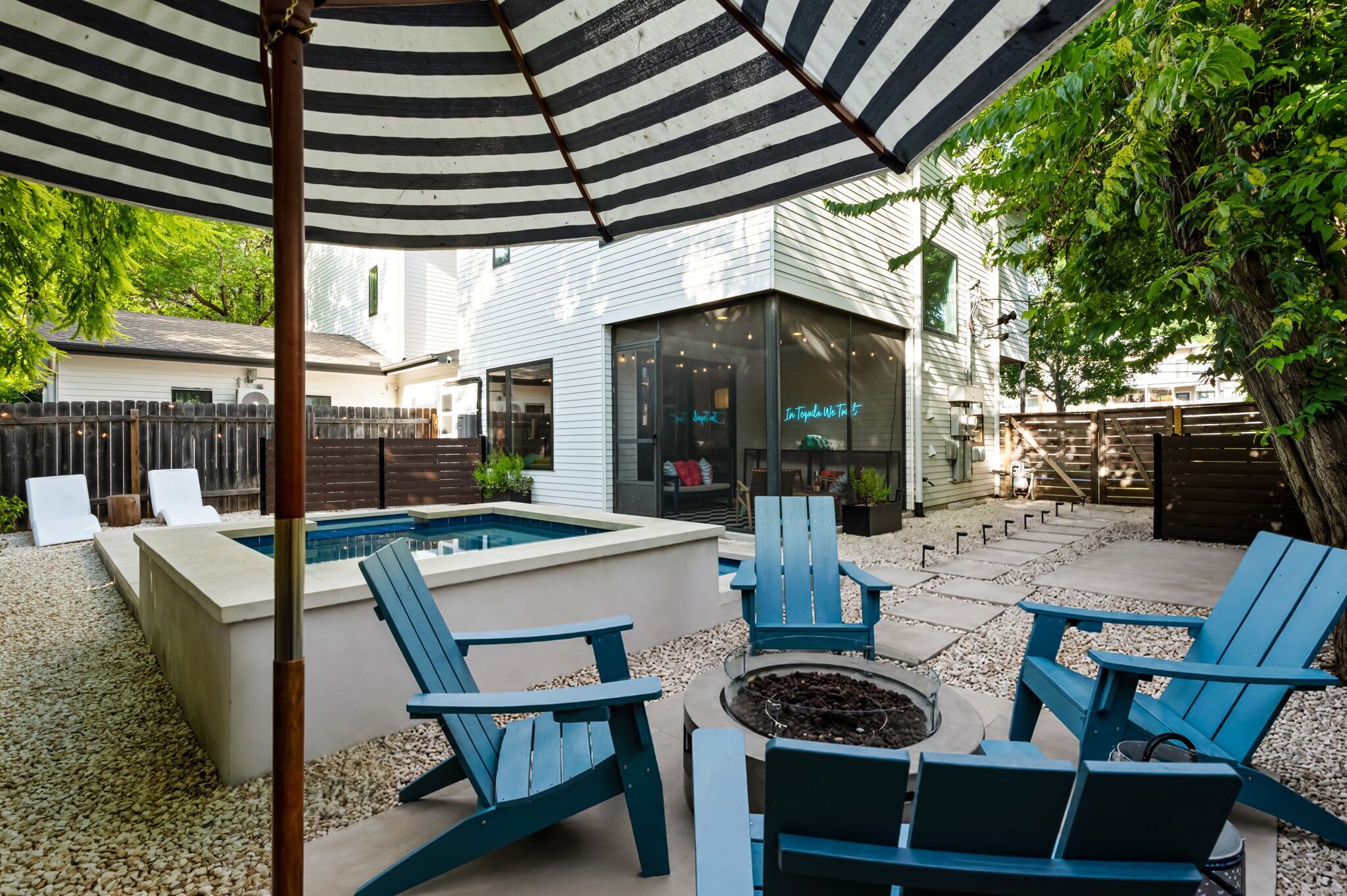 A backyard with a pool, blue Adirondack chairs, and a fire pit.