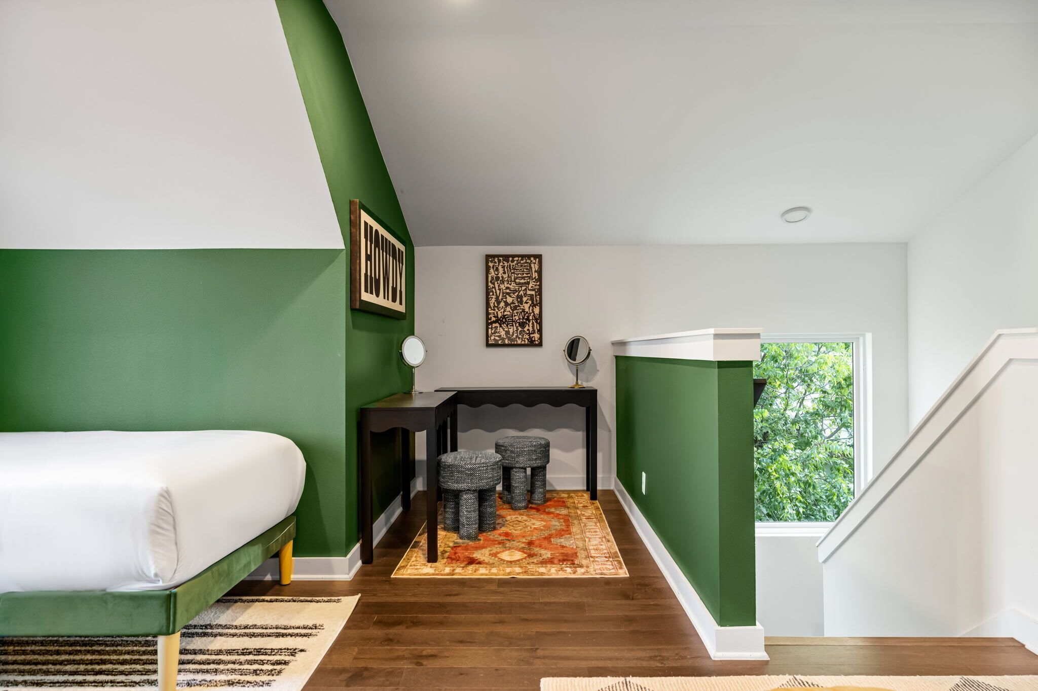 Une chambre à coucher comprenant un lit, un bureau avec deux tabourets, un miroir et une œuvre d’art accrochée au mur.