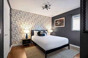 A modern bedroom with a geometric-patterned wall, a bed with a black frame, two bedside tables with lamps, and a ceiling fan. - Rainey Escape / Pool / Hot Tub / Fire Pit / DT ATX (Austin)