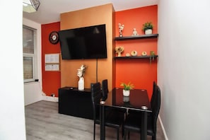 Ein moderner Essbereich mit einem schwarzen Tisch, vier Stühlen, einem an der Wand montierten Fernseher und Regalen mit Dekoration.