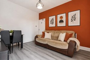 A living room with a brown sofa, a dining table with chairs, and a white door. - Spacious 4BDR | Ideal for Contractors |City centre (Coventry)