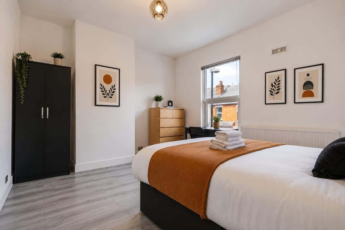 A modern bedroom with a large bed, a wardrobe, a desk, and a window with a view.
